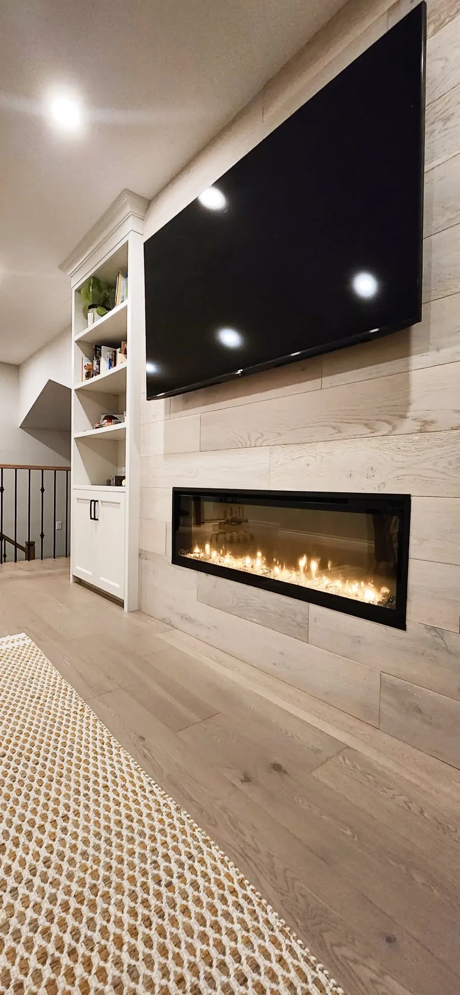 The finished fireplace wall from the side, with the TV above, pale plank panelling and a white bookshelf.