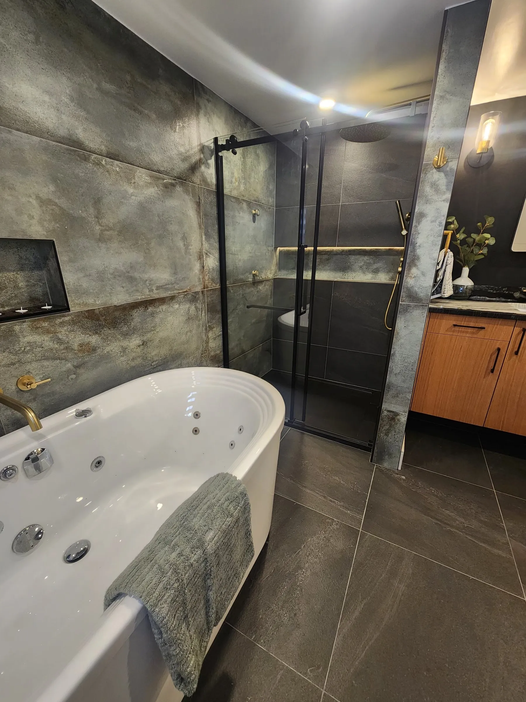 A bathroom with a freestanding tub, large grey stone-look tiles and a glass shower