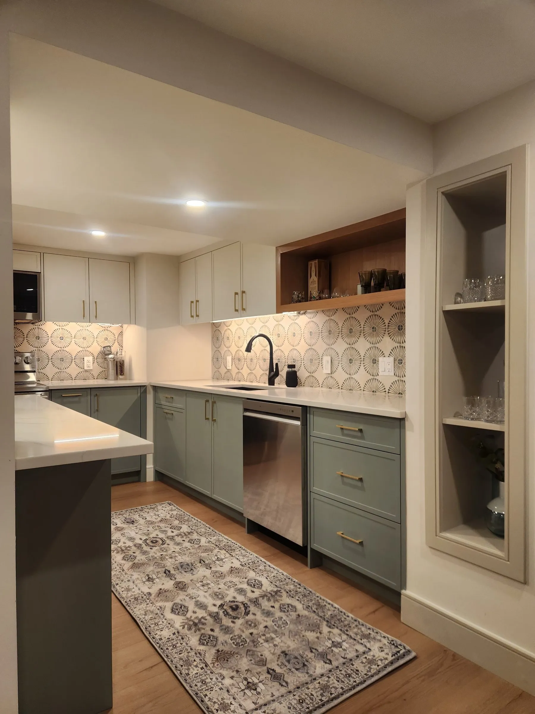 A kitchen with sage green cabinets, a patterned backsplash and a built-in display niche