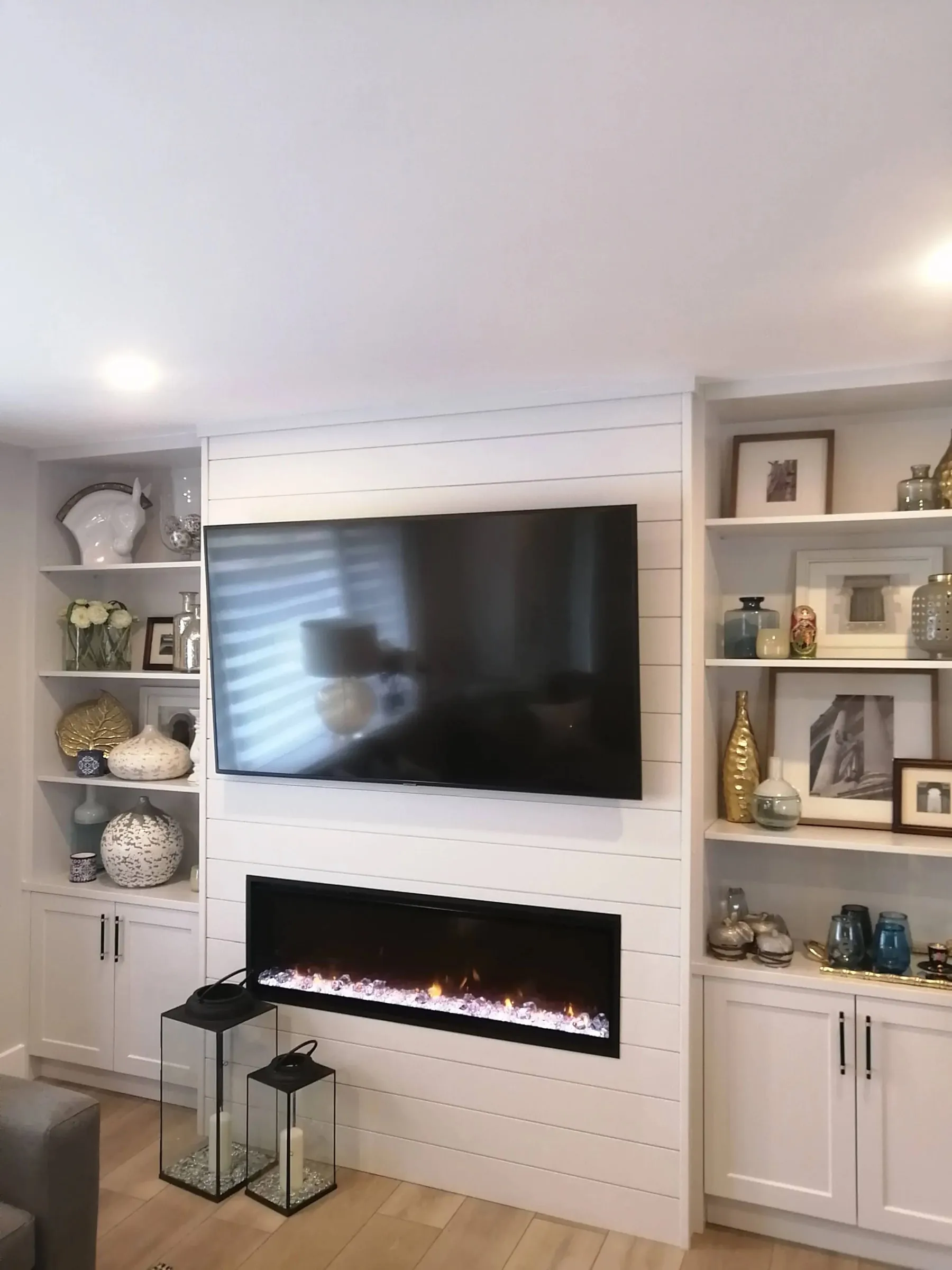 A living room wall with a linear fireplace, white shiplap and built-in shelves on both sides