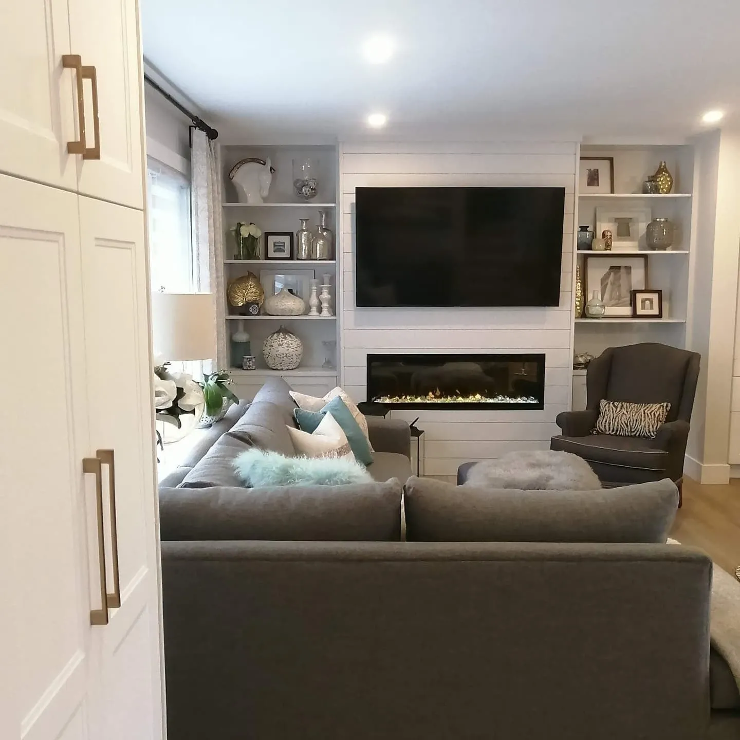 The living room seen past tall white cabinets, with a TV and fireplace centred between built-in shelves.