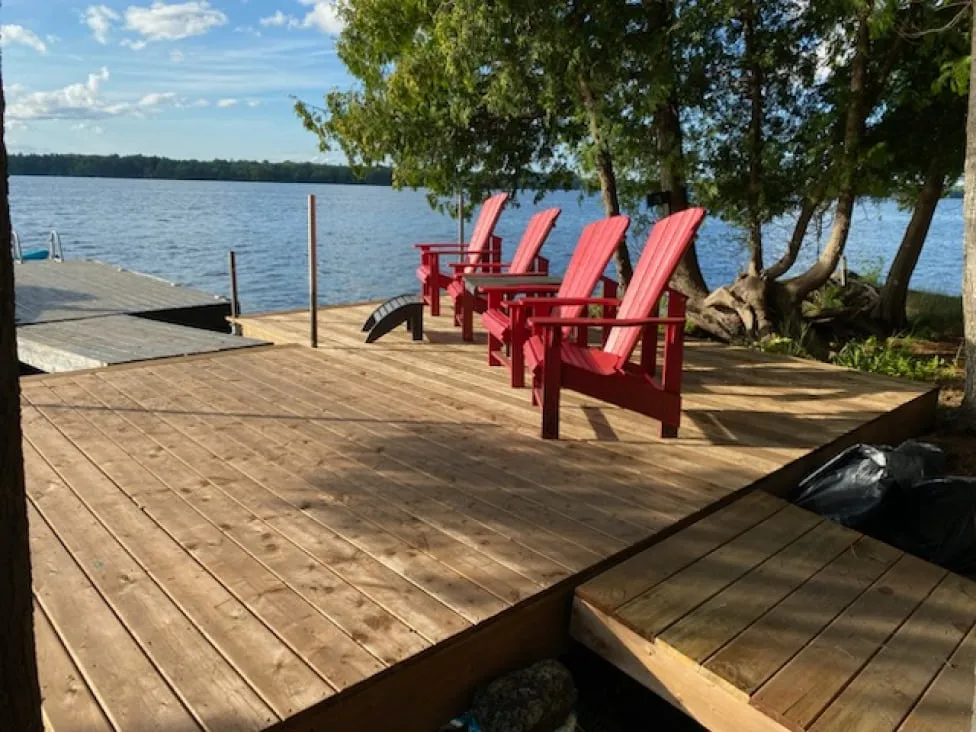 The finished dock with fresh wood boards, four red lounge chairs and a wide lake view.