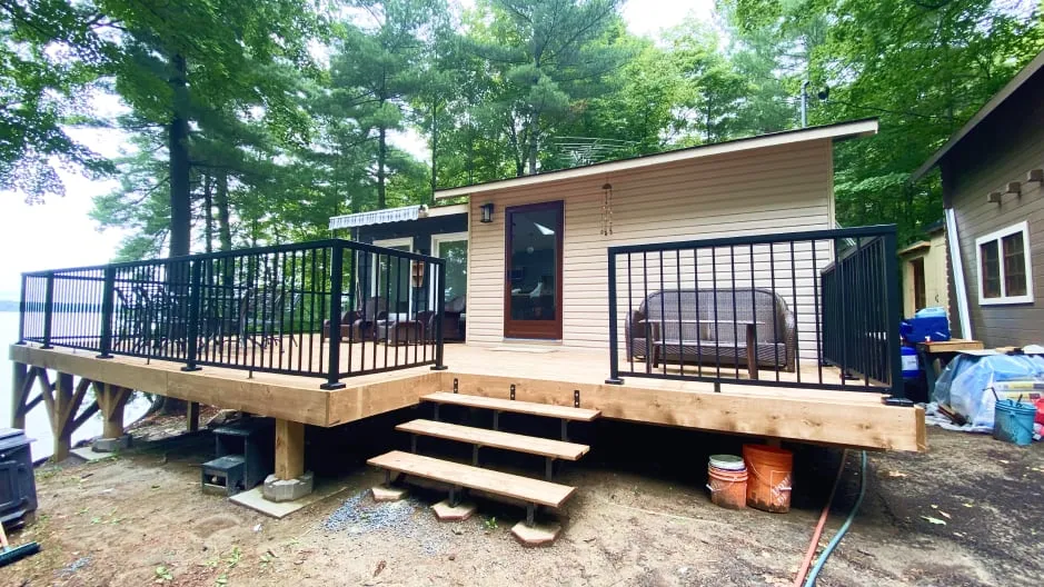 The finished deck with black metal railings and open steps, along beige siding and a brown door.