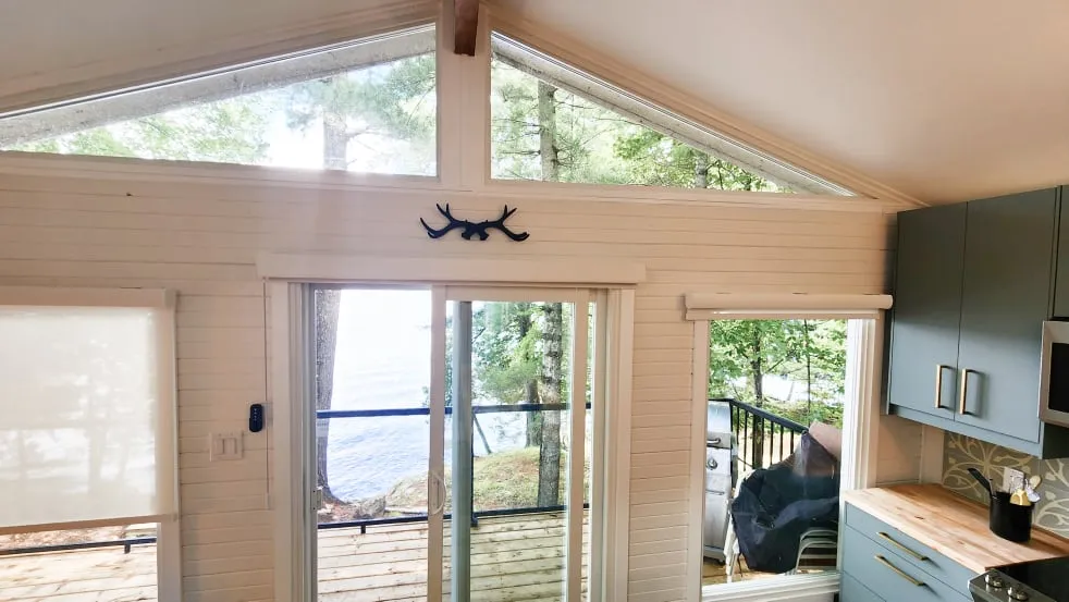 A white panelled wall with triangular gable windows over a sliding glass door facing the lake.