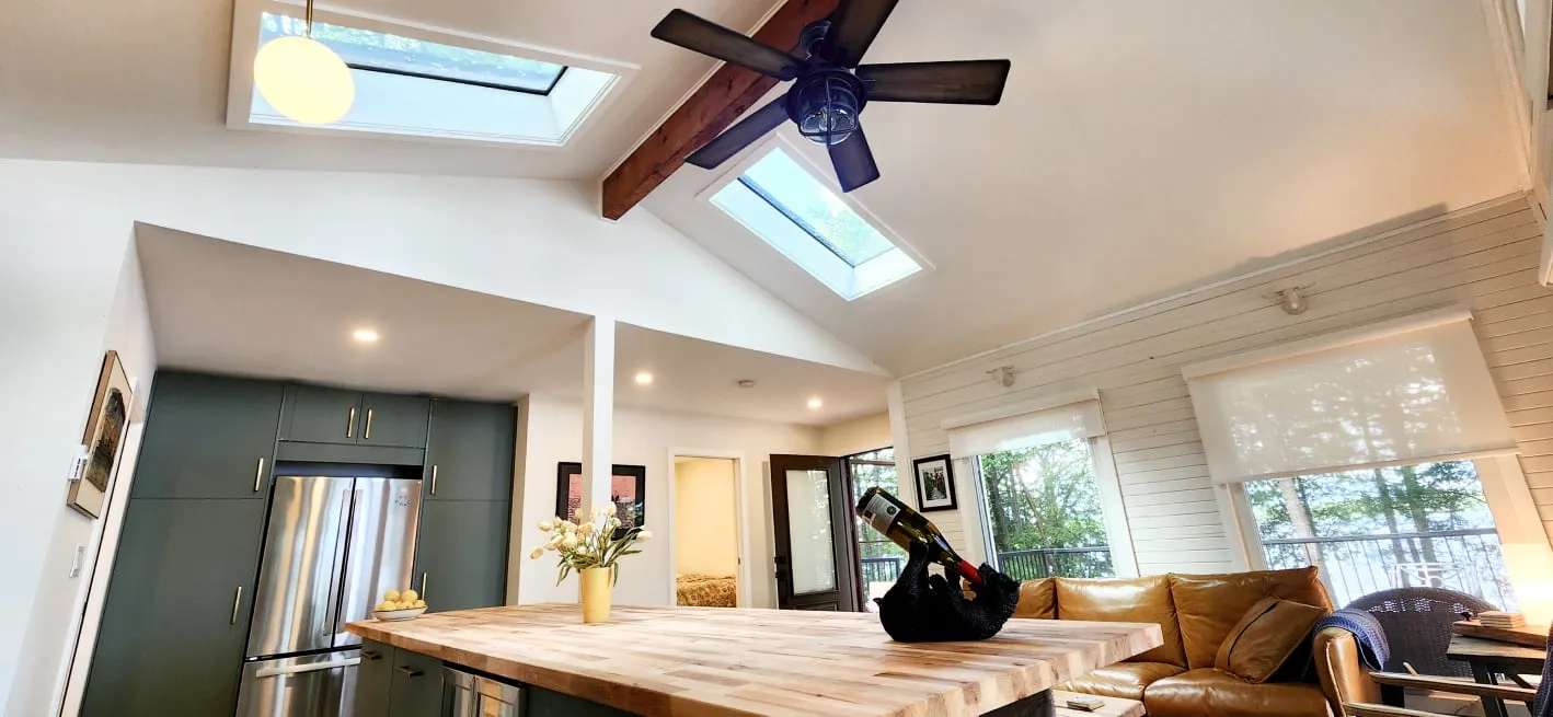 Two skylights in a vaulted white ceiling with a wood beam and fan, above a wood-topped kitchen island.