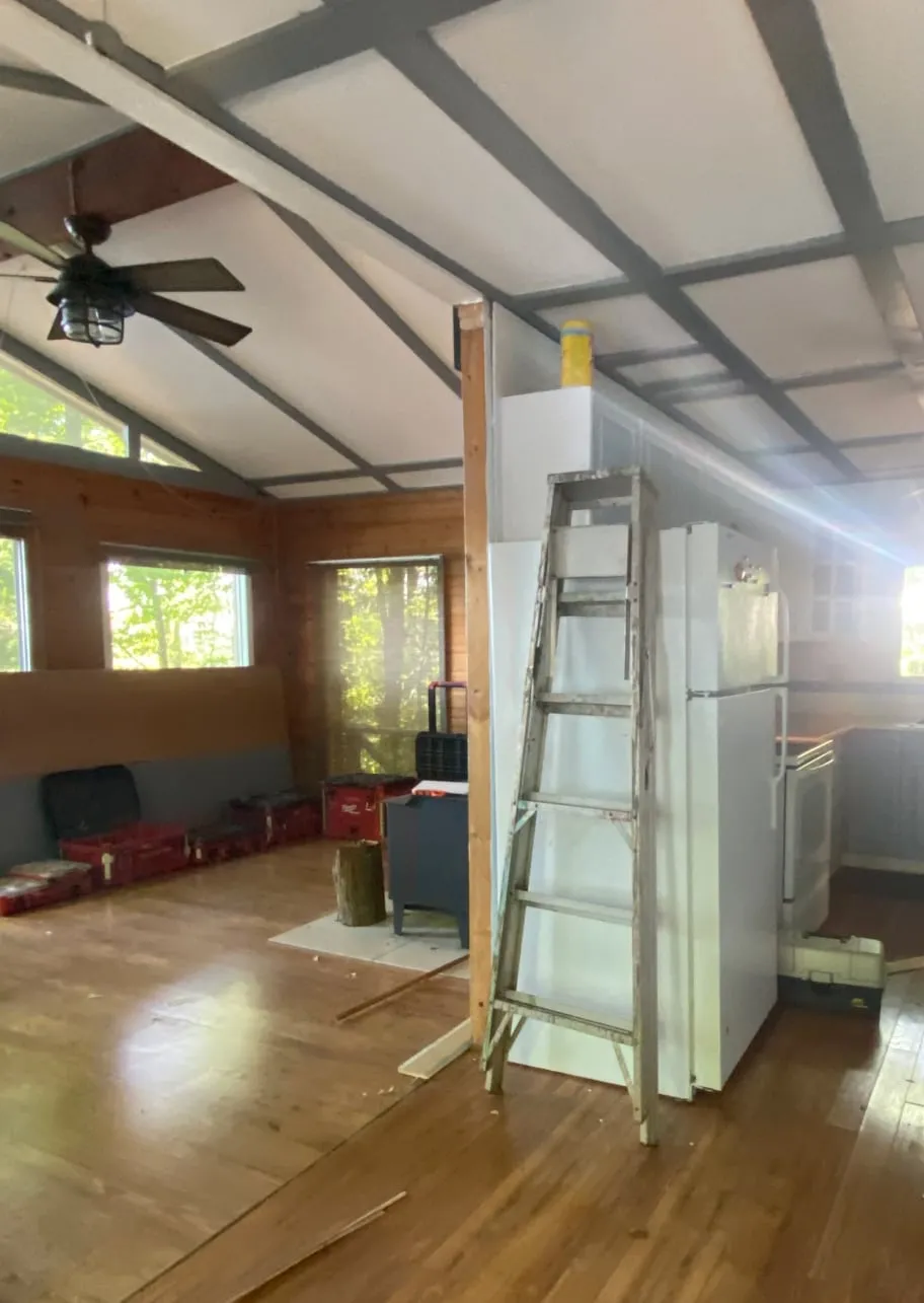 The cottage interior before the work, with a beamed ceiling, wood-panelled walls, an old white fridge and ladder.