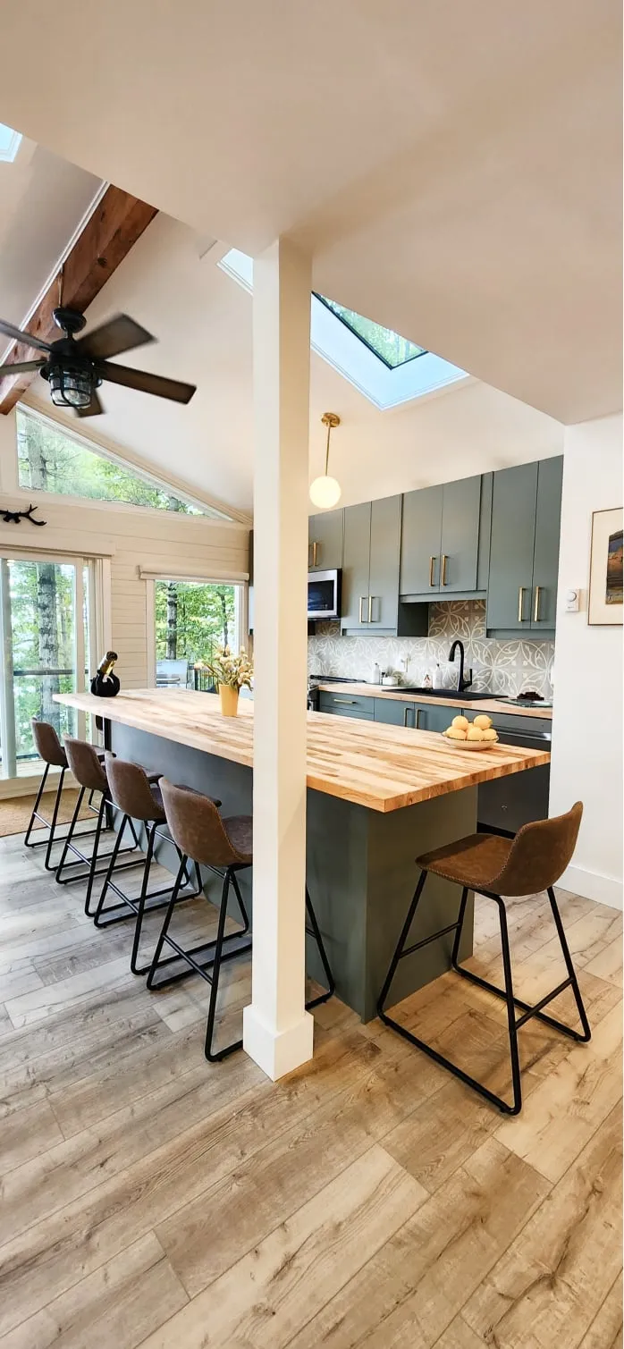 A long wood-topped island with a sage green base and brown bar stools under a vaulted, skylit ceiling.