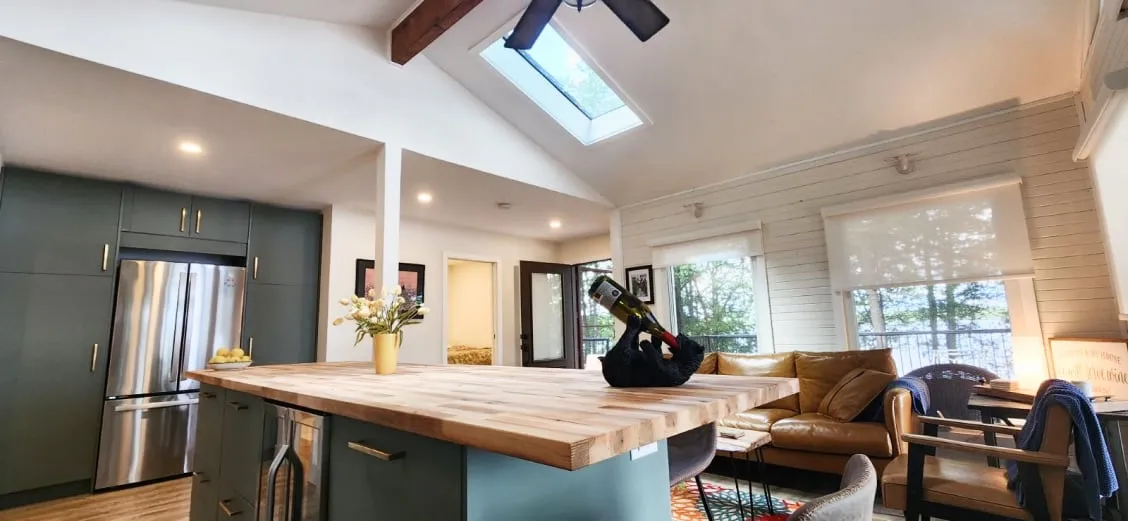 The open kitchen and living area, with green cabinets, a stainless fridge, the island and a skylight above.