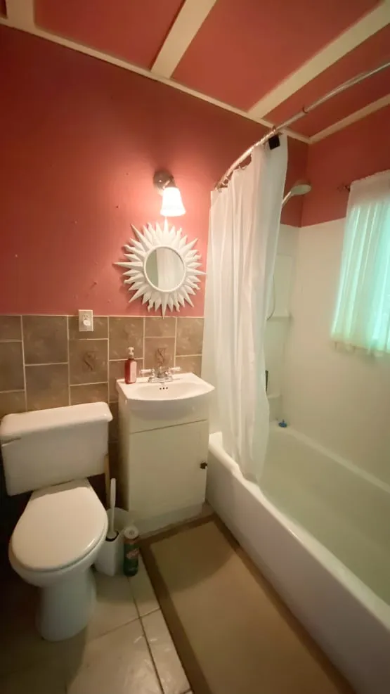 The old bathroom with pink walls, a small white vanity, toilet and a tub with a shower curtain.