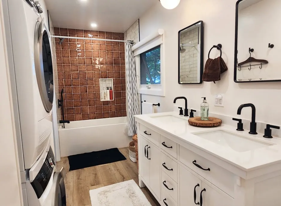 The finished bathroom, with glossy rust-brown tile around the tub and a white double vanity with black taps.