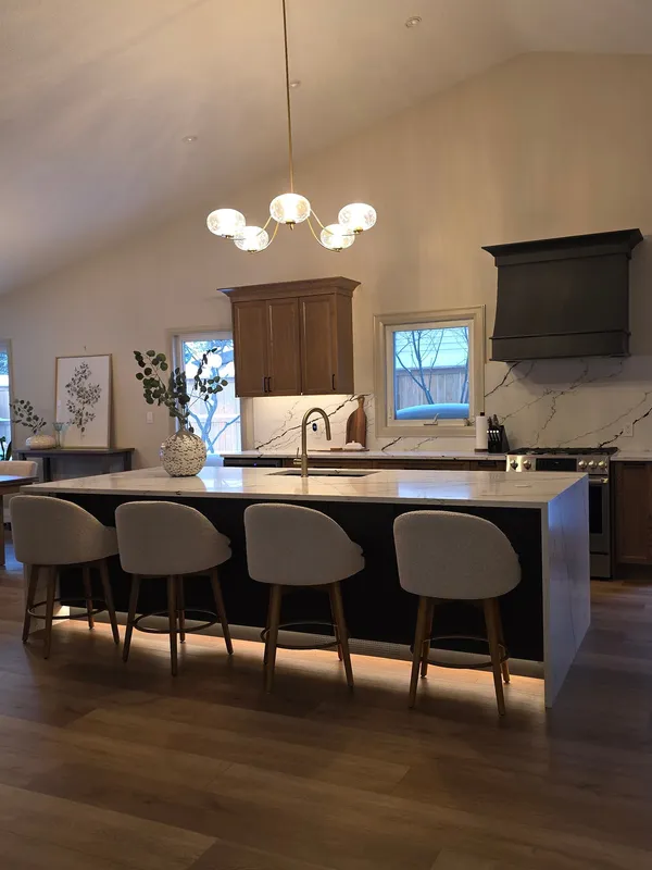 The kitchen under a vaulted ceiling: a long island with four upholstered stools, a globe chandelier above and a black range hood beyond.