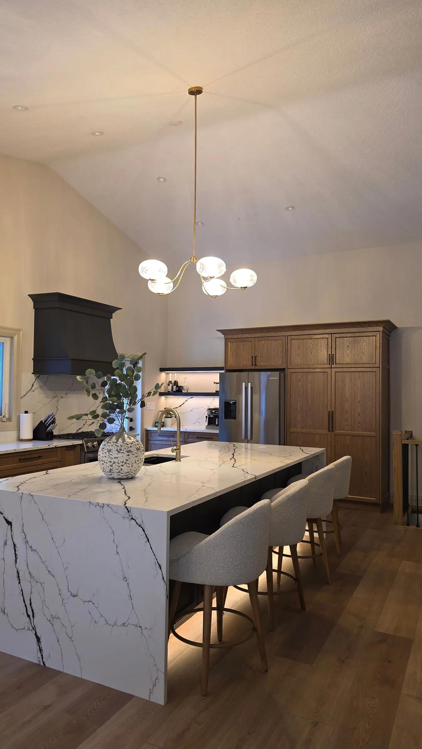 The island's white counter with bold dark veining wrapping down its end, with wood cabinets and a stainless fridge behind.