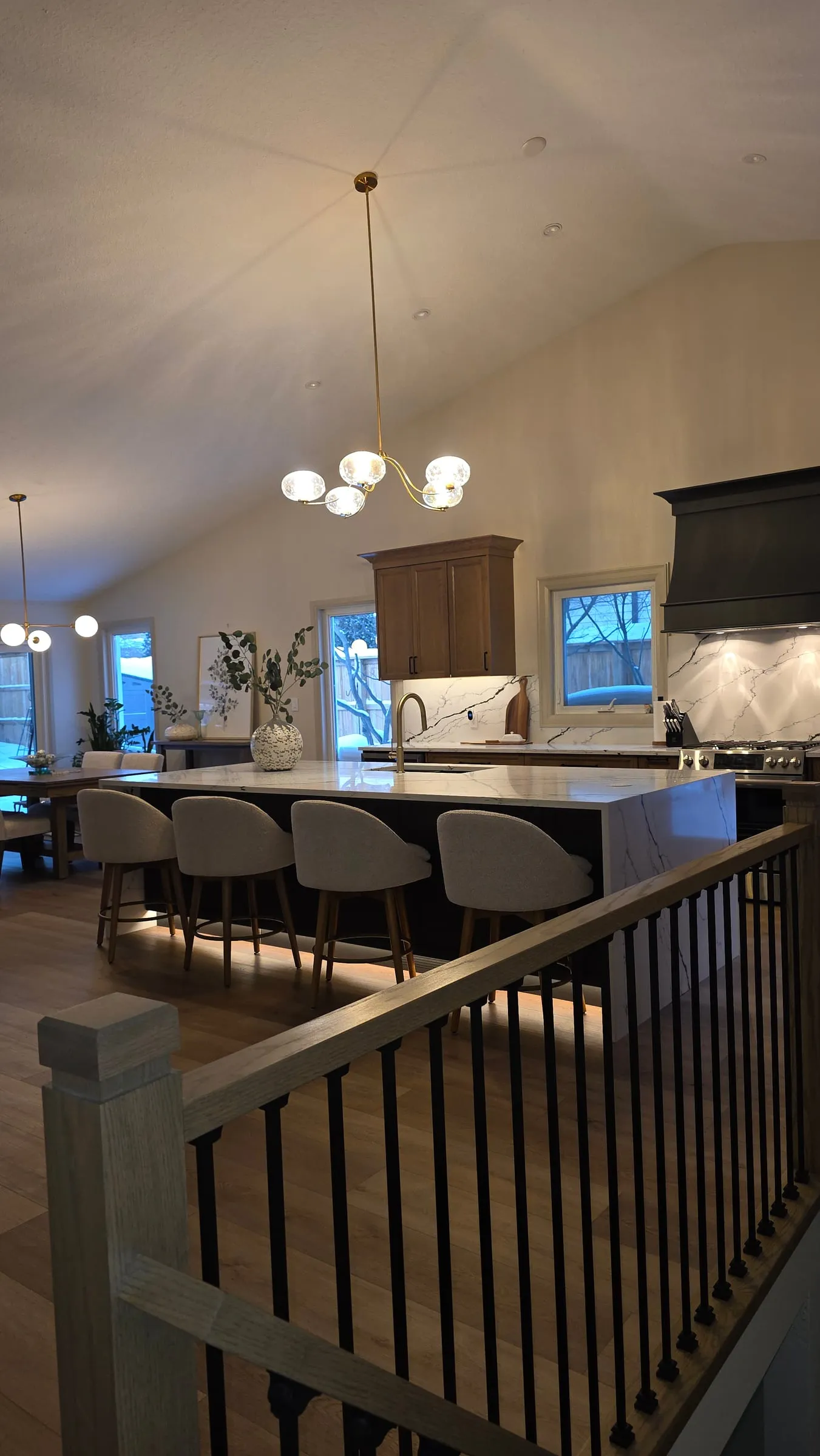 The kitchen and dining area seen from the top of the stairs, past a wood railing with black spindles.