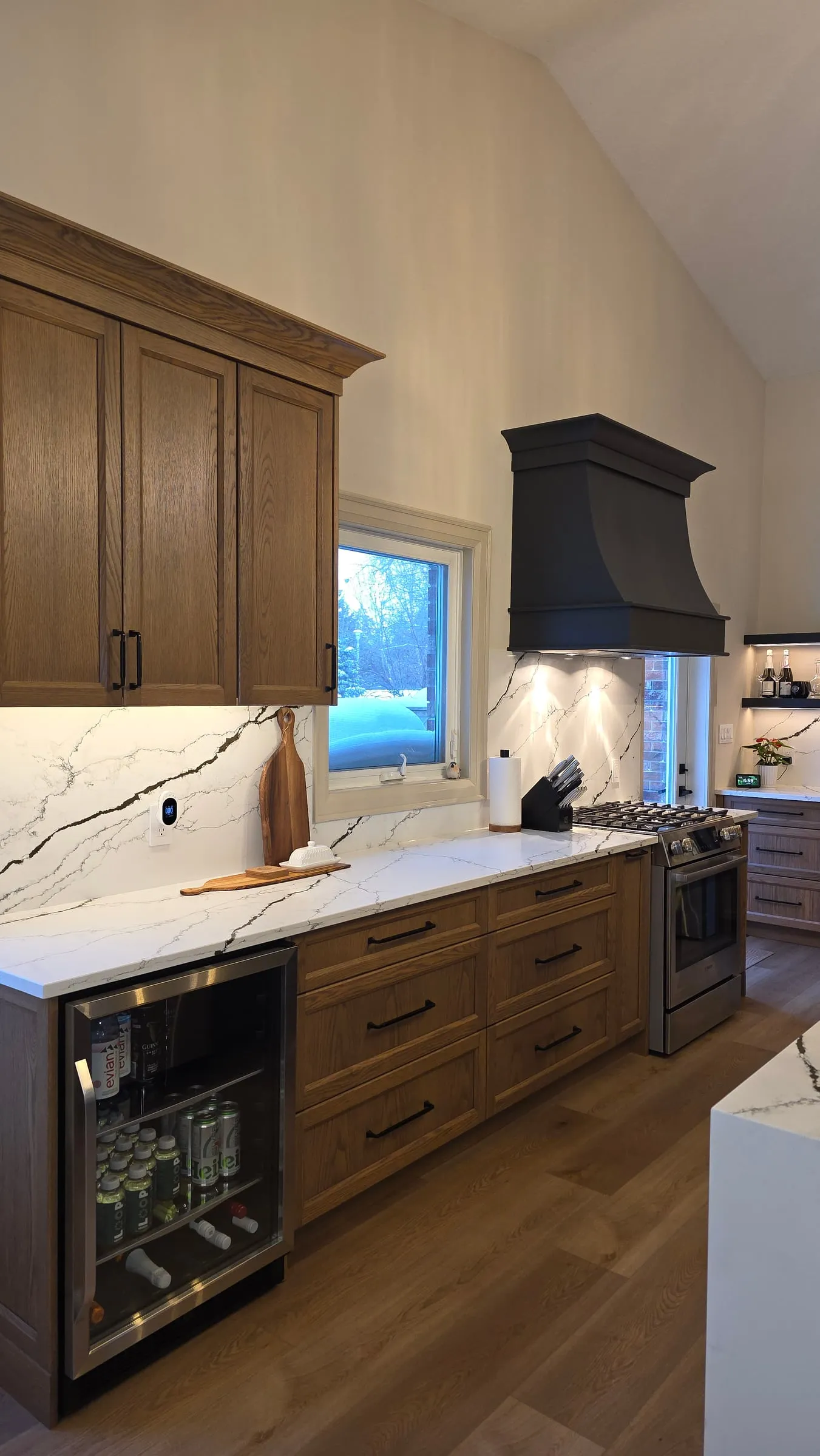 Wood base cabinets with black pulls, a glass-front beverage fridge, and a window over the counter.