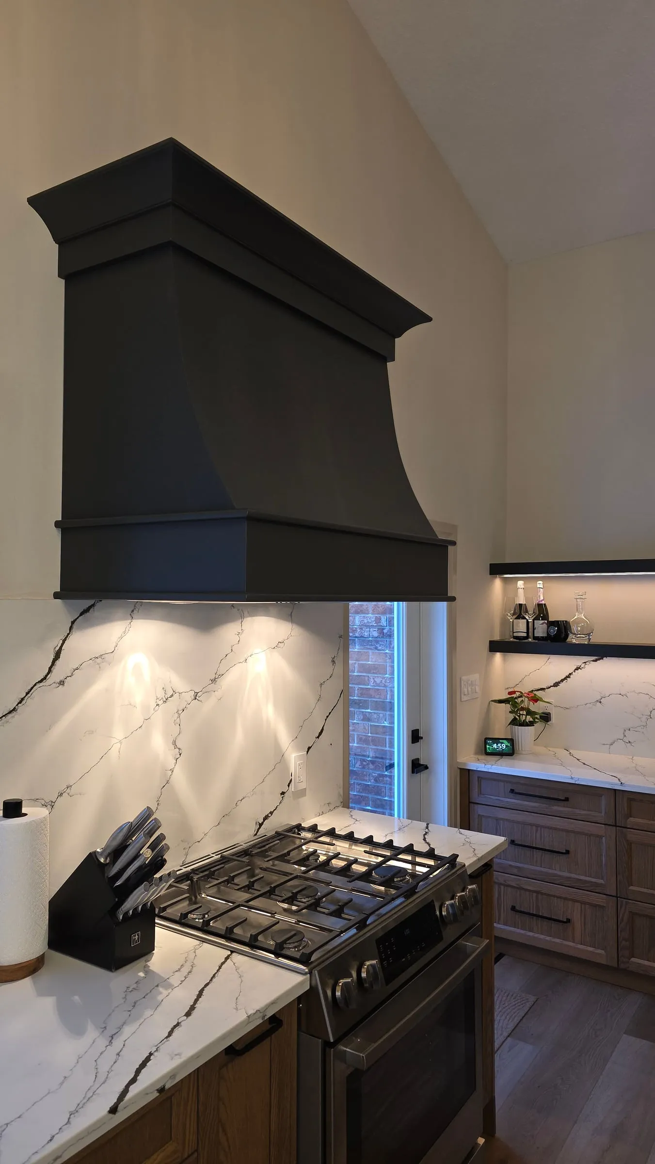 A black range hood over a gas range, with a veined white backsplash and a knife block on the counter.