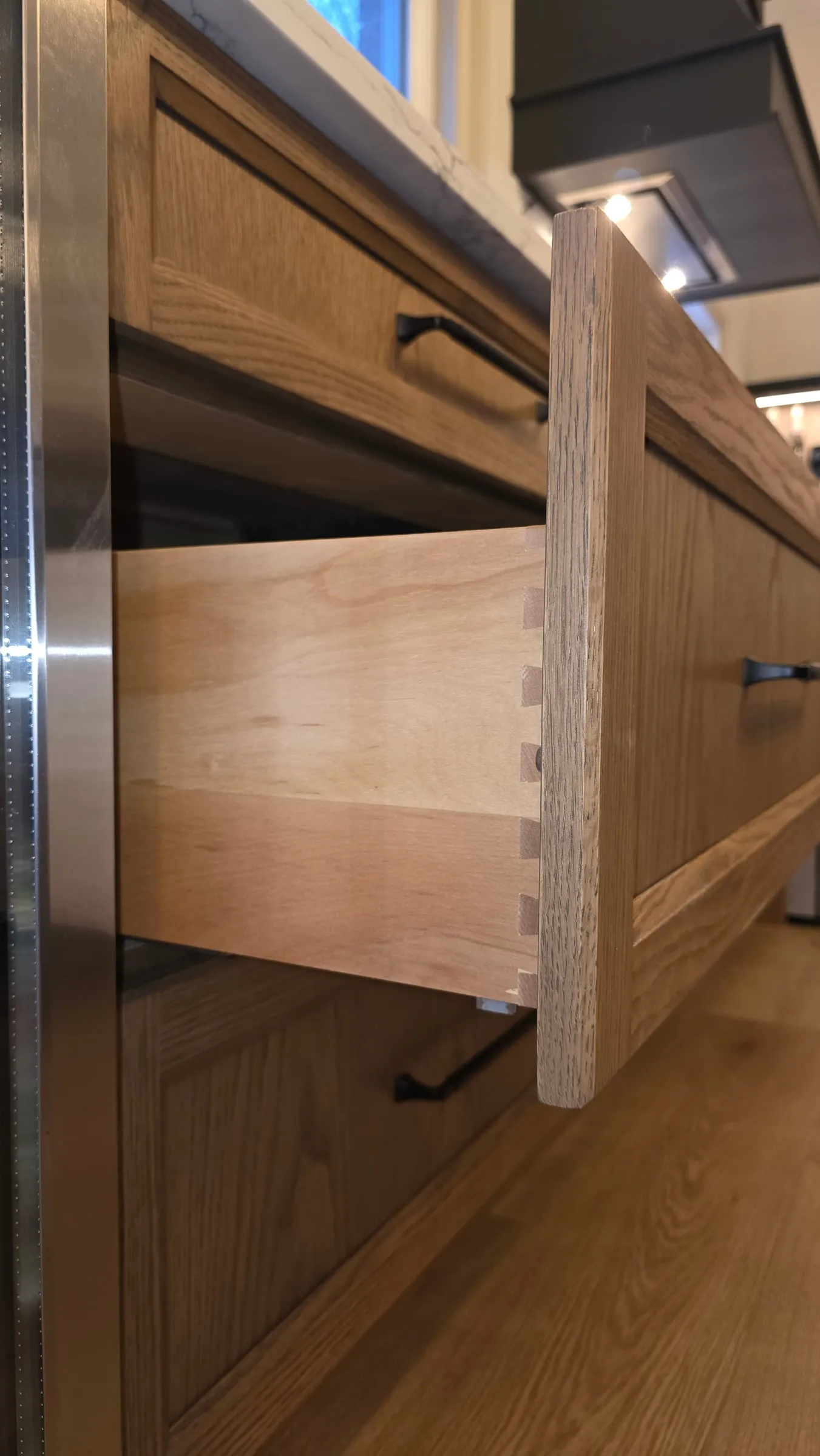 An open drawer showing its dovetail joints, below a wood drawer front with a black pull.