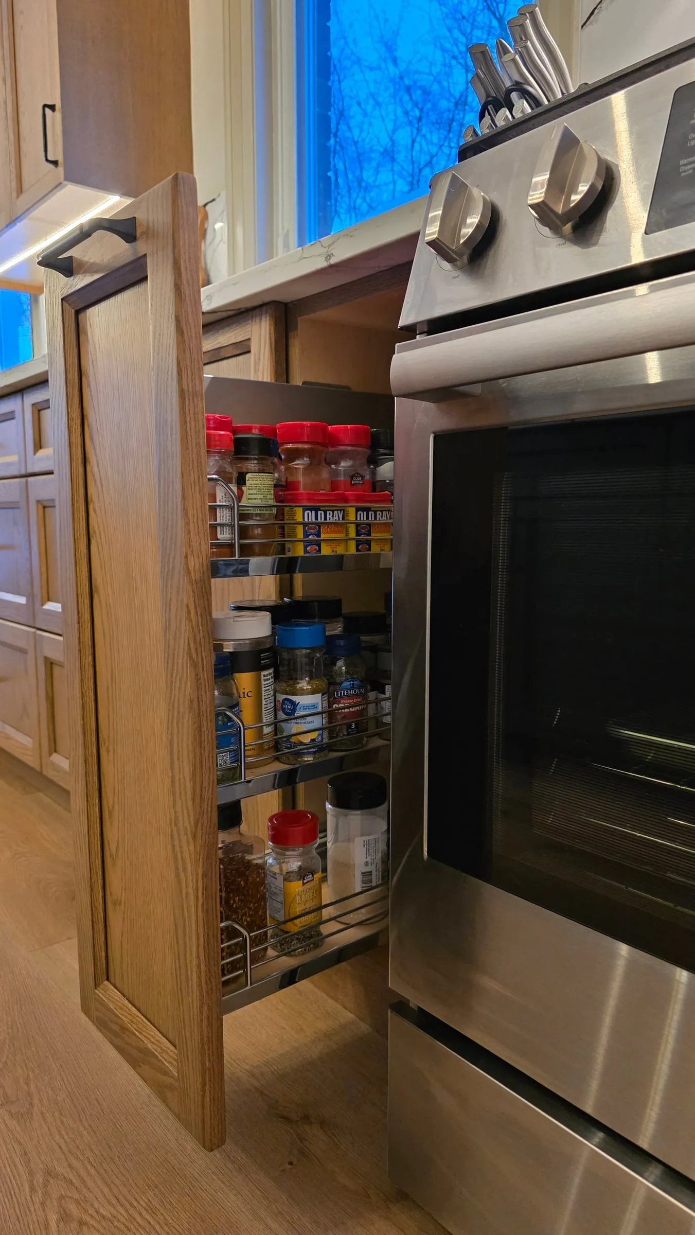 A narrow pull-out spice rack beside the range, open to show rows of spice jars.