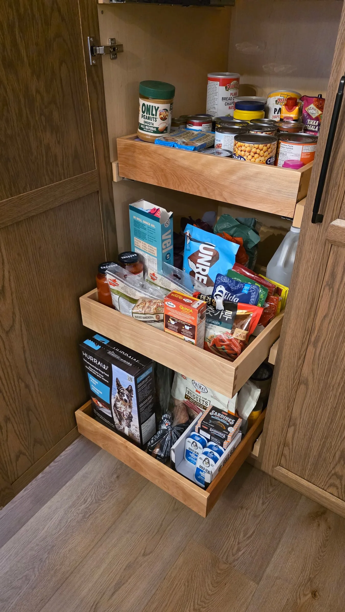 A tall pantry cabinet open to show three pull-out drawers stocked with food.