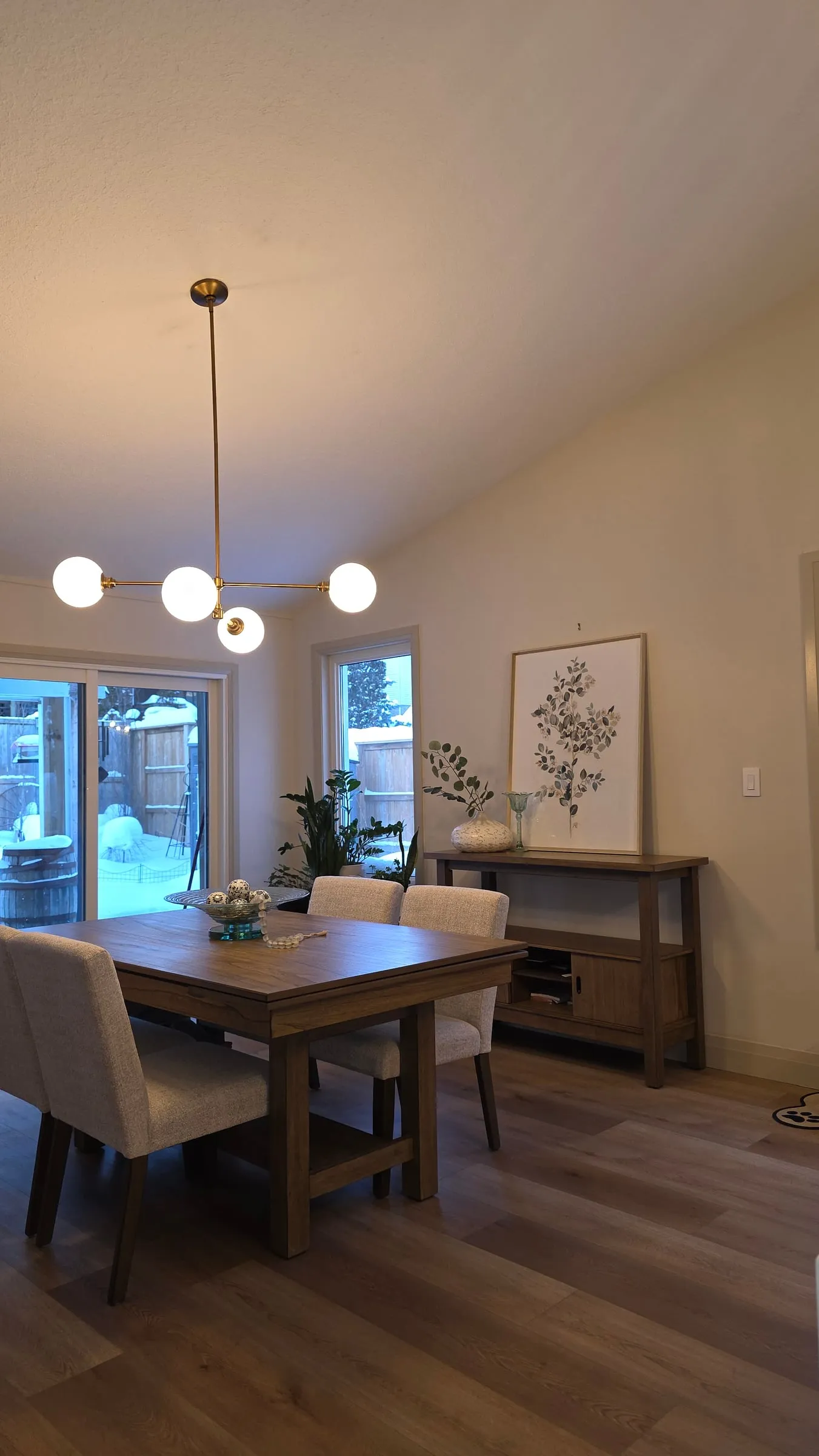 The dining table in front of a glass patio door, with a wood sideboard and a framed botanical print.