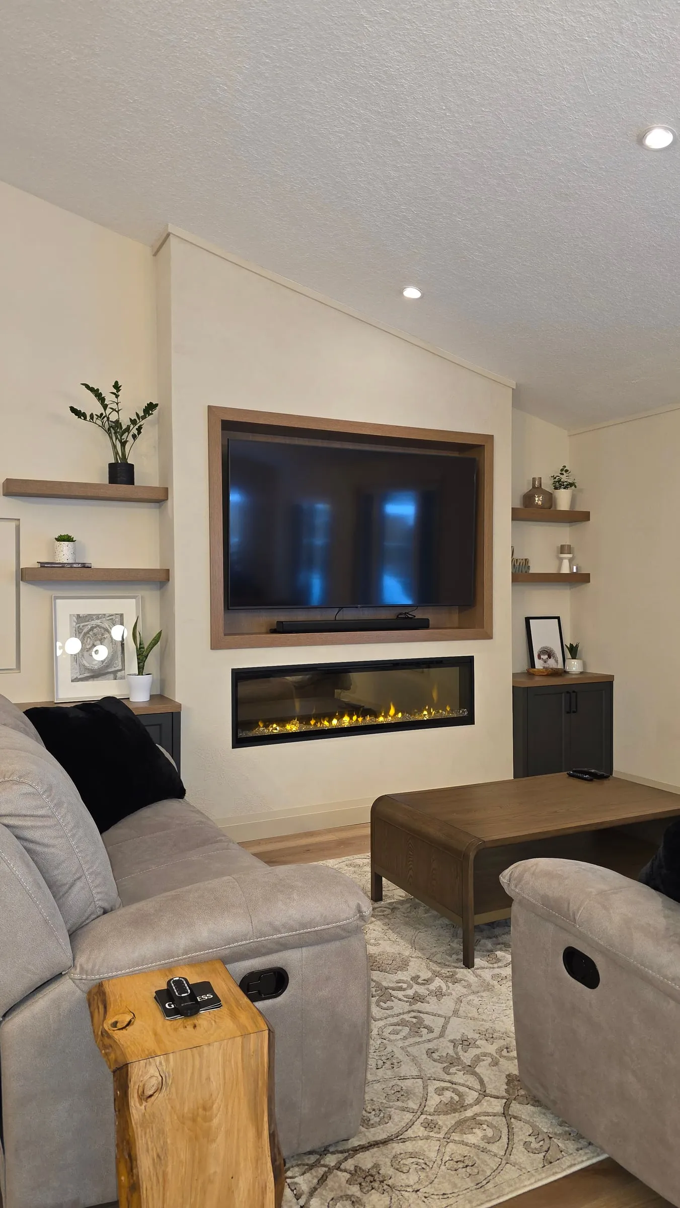 A living room with a TV set into a wood-framed niche, a linear fireplace below it and floating shelves on both sides.