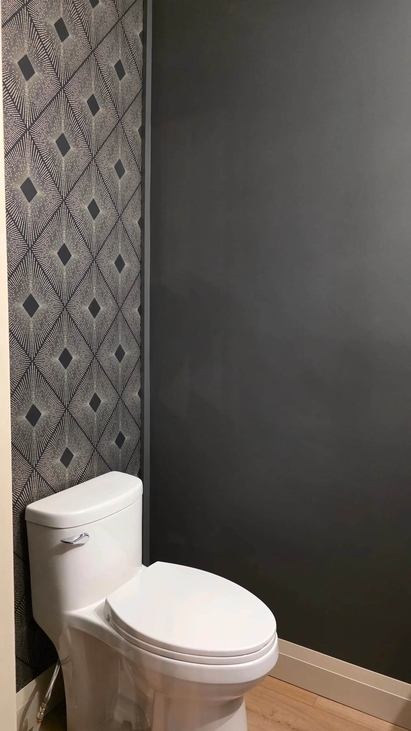 A white toilet beside an accent wall with a dark starburst diamond pattern.